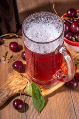 Craft cherry beer or cider alcohol drink mug and bottle on wooden table with fresh ripe cherries, copy space