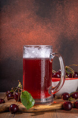 Craft cherry beer or cider alcohol drink mug and bottle on wooden table with fresh ripe cherries, copy space