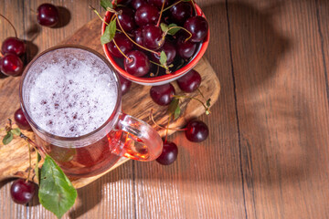 Craft cherry beer or cider alcohol drink mug and bottle on wooden table with fresh ripe cherries, copy space