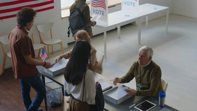 High angle shot of diverse people walking to election inspectors, receiving ballots and going to voting booth at polling place