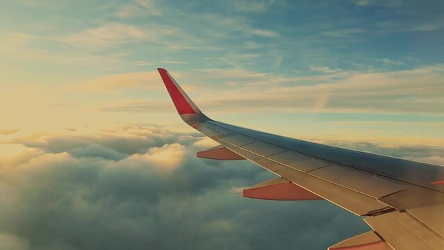 big airplane wing window view flying above the clouds at sunset golden hour view from window