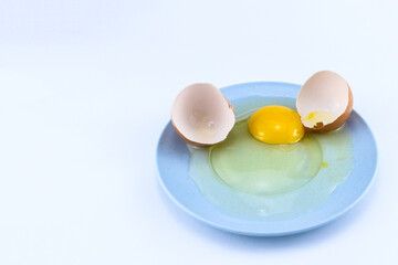 Cracked raw eggs on a small bluish plate with a white isolated background