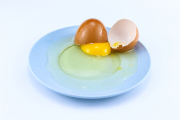 Cracked raw eggs on a small bluish plate with a white isolated background