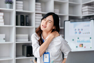 business woman is sitting at a desk with a laptop and a pain shoulder in front of her. She is injured and she is in a sad mood