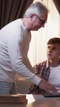 Vertical video. Gaming addiction. Strict father. Parent punishment. Overjoyed son playing online shooter serious scolding dad closing laptop at home.