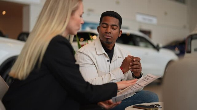 Female car dealer consulting doubtful black buyer, handing over purchase agreement for review at showroom. Serious African client reading car purchase contract before signing in dealership office.