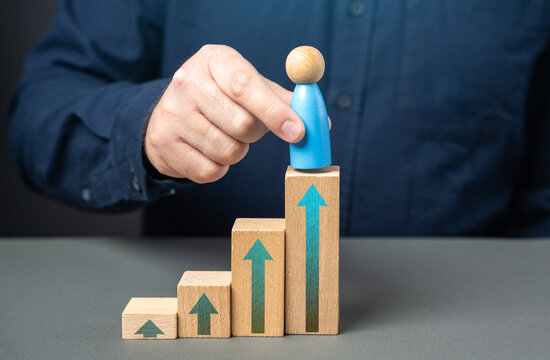 A man places a figurine of a man at the top of the stairs. Promote a worker for excellent performance. Reach the highest level of your career. Achieve success.