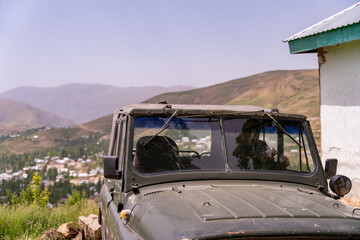 A green jeep is parked on a hillside with a view of a village