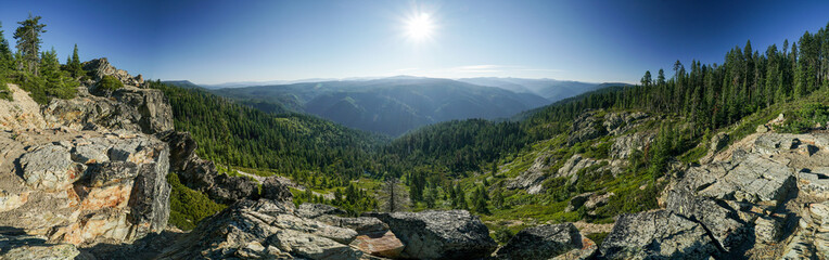 A panoramic view of a mountain range with a bright sun shining down on the trees