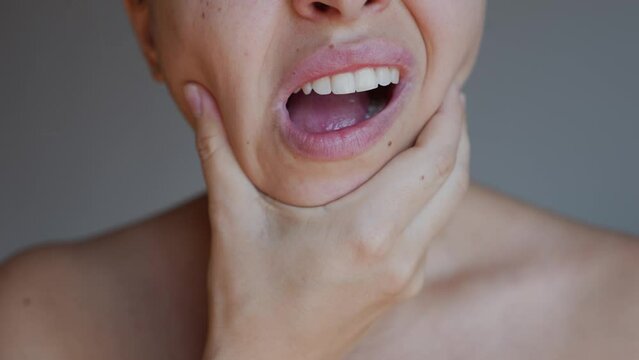 Cropped shot of a young woman suffering from jaw pain holding her chin on a dark grey background. Inflammation of cervical lymph nodes, Diseases of ENT organs, facial, trigeminal nerve, toothache