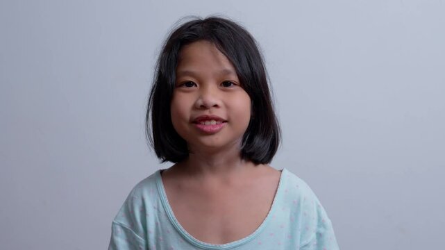 Portrait Funny little asian girl big smiling child looking at camera and pointing her cheeks, enjoying childhood testimonial concept,  Positive child, 4k footage, Slow Motion Portrait