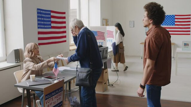 Diverse voters queuing in line, getting ballots and going to booths at polling place on Election day