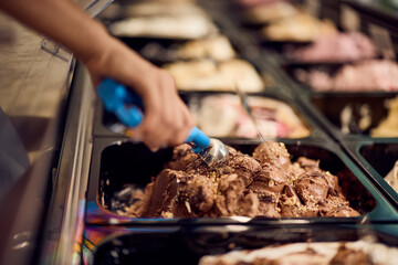 Chocolate ice cream in a container in a glass case, using a scoop of it.