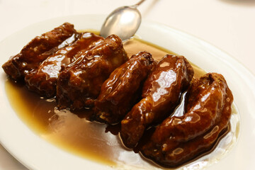 close up of six pieces of Chinese soy sauce sweet and sour pork rib with brown gravy sauce on a white plate.