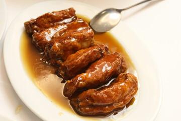 close up of six pieces of Chinese soy sauce sweet and sour pork rib with brown gravy sauce on a white plate.