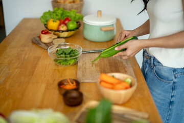 A woman is cutting a cucumber on a wooden cutting board