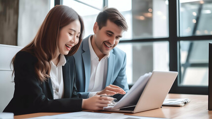 This image portrays two people in a professional setting, engaged in a productive discussion while smiling and looking at a laptop.