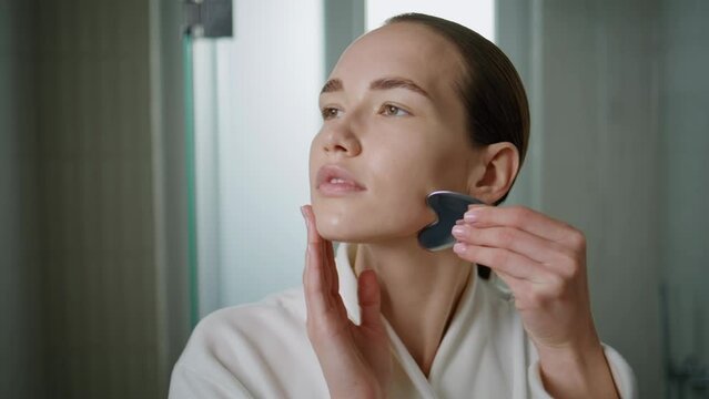 Woman doing gua sha lifting treatment closeup. Serene girl massage face at home