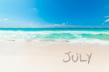 Tropical beach with July written on the sand