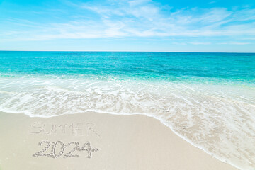 Summer 2024 written on the sand in a beach with turquoise water