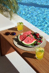 Juicy red watermelon, berries and two glasses of iced lemonade with mint on sunny day by the poolside. Summer vibe concept. Close up, copy space, background.