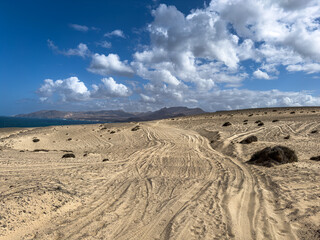 Fahrspuren im Sand mit Bergen und Himmel im Hintergrund