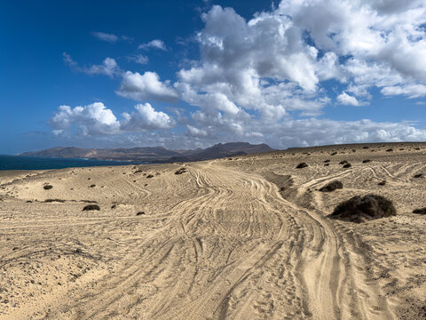 Fahrspuren im Sand mit Bergen und Himmel im Hintergrund