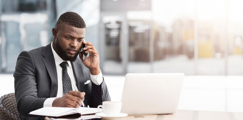 African Business Guy Multitasking Talking On Cellphone Working On Laptop And Taking Notes Sitting In Outdoor Cafe. Busy Lifestyle Concept