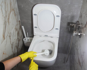 Washing and cleaning the toilet with a brush and detergent to remove dirt, limescale and urinary stone, close-up. Cleaning company services