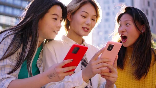Group of only Chinese generation z women sitting together looking and searching for information on mobile phone outdoors. Young urban Asian girls friends talking using smartphone enjoying sunny day
