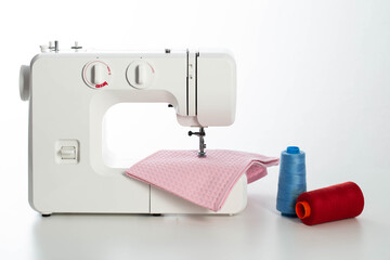 Modern automatic white sewing machine with pink fabric and multi-colored spools of thread on the table. White background. Tailoring and clothing repair services. Copy space for text