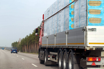 A truck with a semi-trailer transports a bulk load of insulation for construction along a country road in the spring. Copy space for text, industry