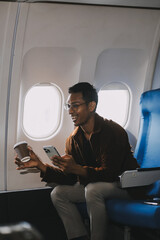 Happy curly man use phone and listens to music headphones on board airplane during flight.