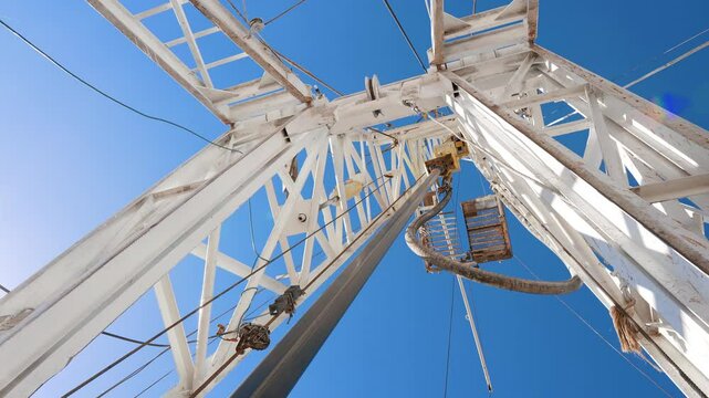 Rotating pole is attached to the white metal tower. Low angle view on the drilling equipment working outdoors.