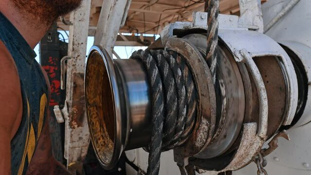 Unrecognized bearded man pulls the rope winded on the metal roller of equipment. Construction or drilling site concept.