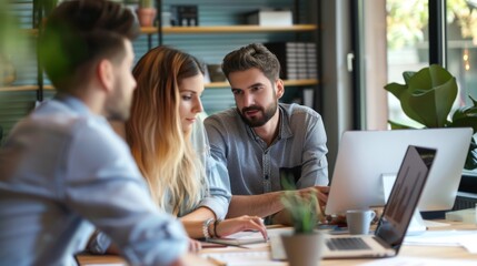 A group of young professionals collaborating on a project in a modern office, engaging in discussion and using laptops and documents.