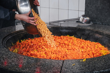 male chef adds chickpeas to a cauldron with carrots to cook traditional oriental Uzbek pilaf in the...
