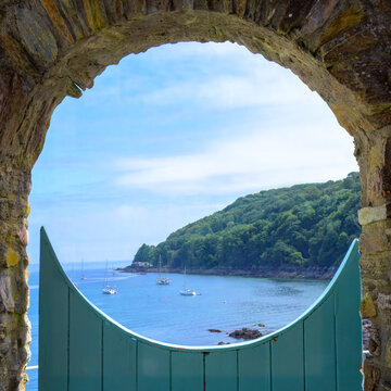 view of Cawsand Bay and the Rame Peninsula through a porthole created in a wall with a gate