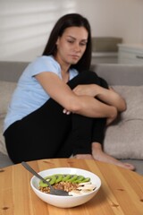 Eating disorder. Sad woman on sofa indoors, focus on granola, kiwi and banana