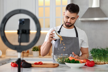 Food blogger cooking while recording video with smartphone and ring lamp in kitchen