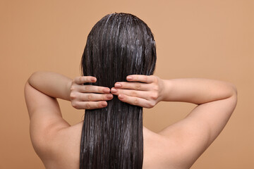 Naklejka premium Woman applying hair mask on beige background, back view