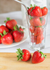 ripe, juicy, red strawberries in a glass and plate on the kitchen table, vertical photo. High quality photo