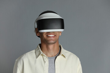 Smiling man using virtual reality headset on gray background