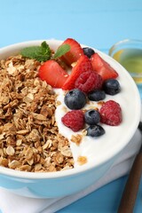 Tasty granola with berries and yogurt in bowl on light blue table, closeup