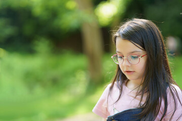 Little cute teenage girl wearing glasses on a blurred summer natural background. Happy childhood concept