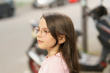 Little cute teenage girl wearing glasses on a blurred summer city background. Happy childhood...