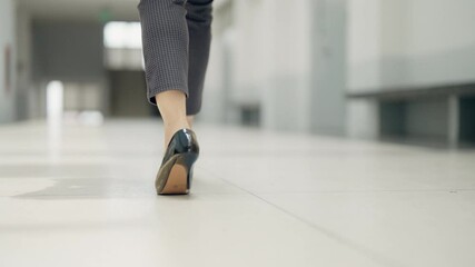 A woman wearing high heels walks down a hallway. Concept of elegance and sophistication, as the woman's attire and posture suggest that she is attending a formal event or going to work