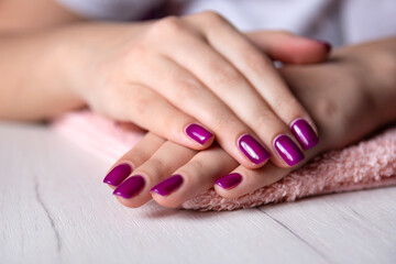 Fototapeta premium Young female hands with purple manicure placed one over the other posing on a white table in a studio, concept of manicure.