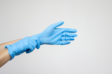 A female doctor or nurse puts on blue medical gloves to perform a procedure. Isolated on a light gray background with copy space. Medicine and healthcare concept. Injections and vaccinations, surgery