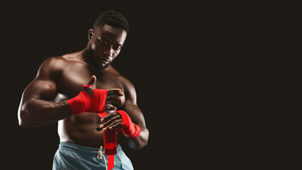 A muscular boxer wraps his hands with red tape in preparation for a fight.